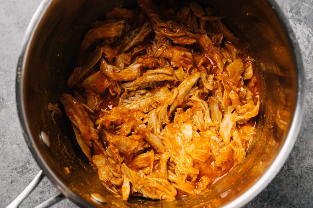 Shredded chicken tossed with buffalo sauce in a pot.