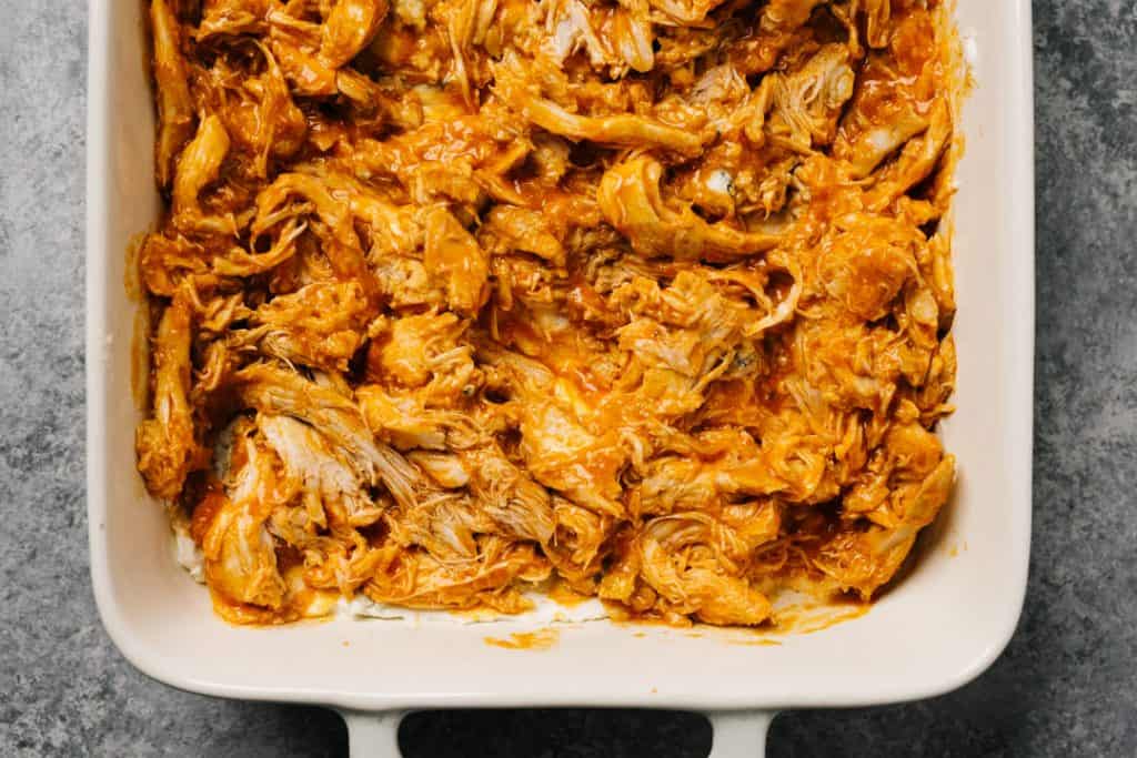 Buffalo shredded chicken over a cream cheese and blue cheese layer in a casserole dish.