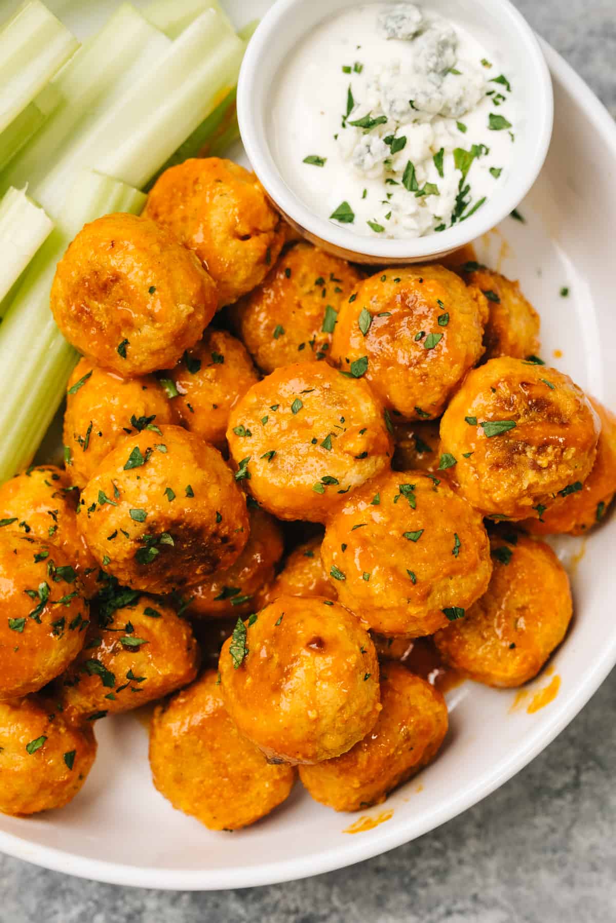 Buffalo chicken meatballs in a large white serving dish with celery sticks and a small dipping bowl of blue cheese dressing.