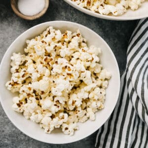 Several bowls of homemade popcorn on the stovetop with a small dish of sea salt and a striped linen napkin.