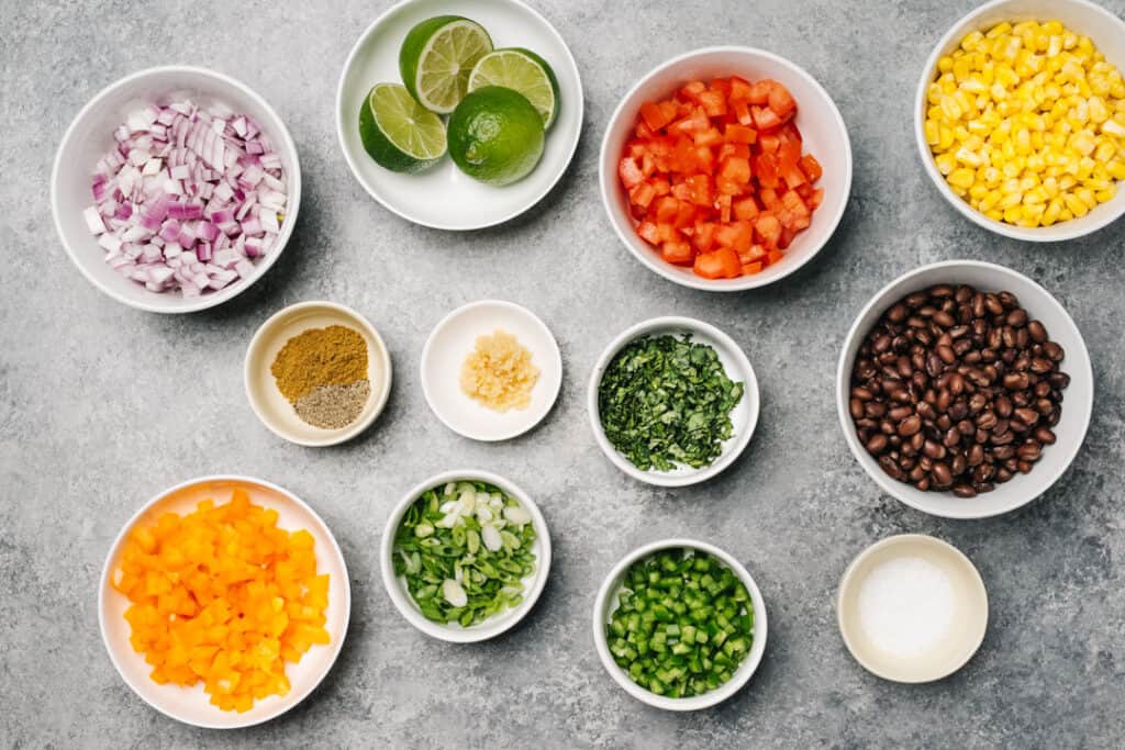 The ingredients for black bean and corn salsa in small bowls on a concrete background.