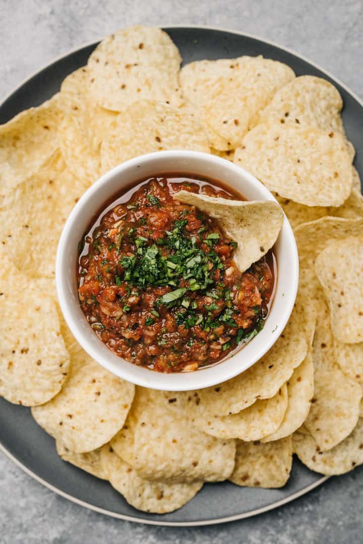 A small bowl of blender salsa on a black plate, surrounded by tortilla chips.