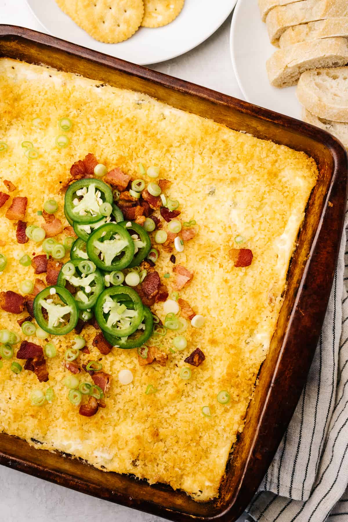 Jalapeno popper dip in a casserole dish, surrounded by Ritz crackers and sliced bread.